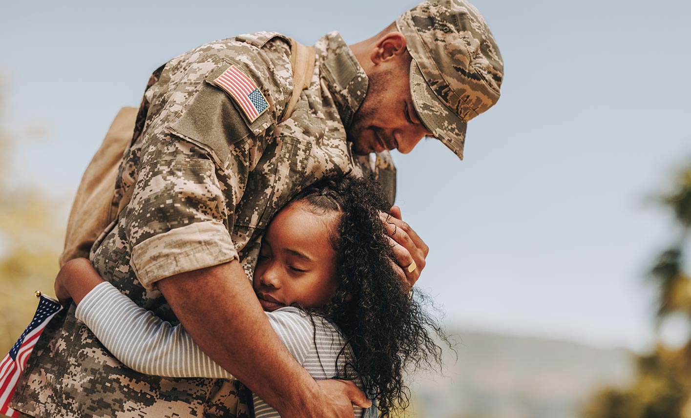 A father in military uniform hugs his young daughter.